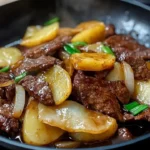 Beef and potato stir fry with vibrant vegetables cooked in a skillet.