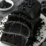 Delicious slice of black velvet cake roll with cream filling on a white plate.