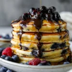 Delicious blueberry pancakes topped with chocolate ganache and berry sauce