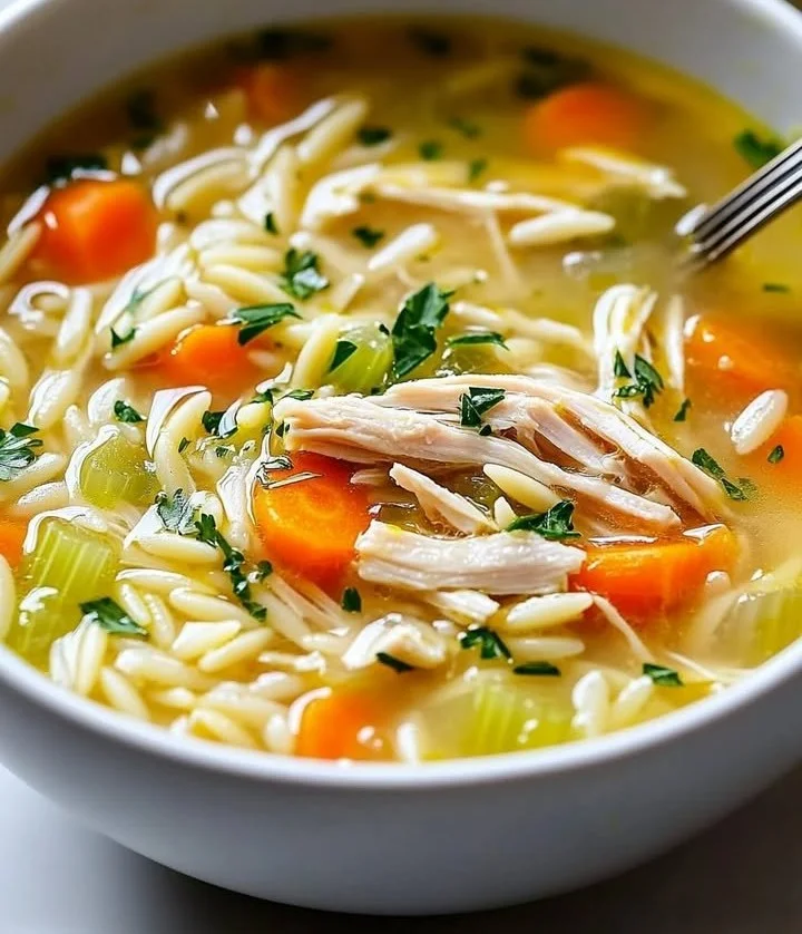 Bowl of cozy Lemon Chicken Orzo Soup garnished with fresh herbs