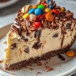 No-bake M&M Snickers cheesecake topped with colorful candies and chocolate drizzle
