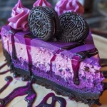 A slice of Purple Velvet Oreo Cheesecake topped with Oreo crumbs and purple frosting.