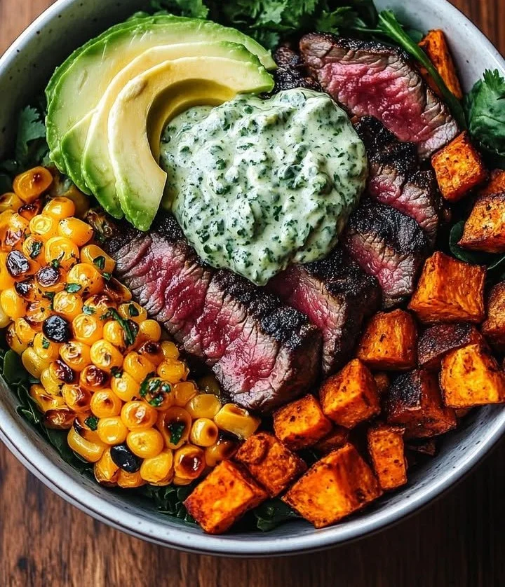 Delicious steak bowl topped with avocado and roasted corn, drizzled with cilantro cream sauce.